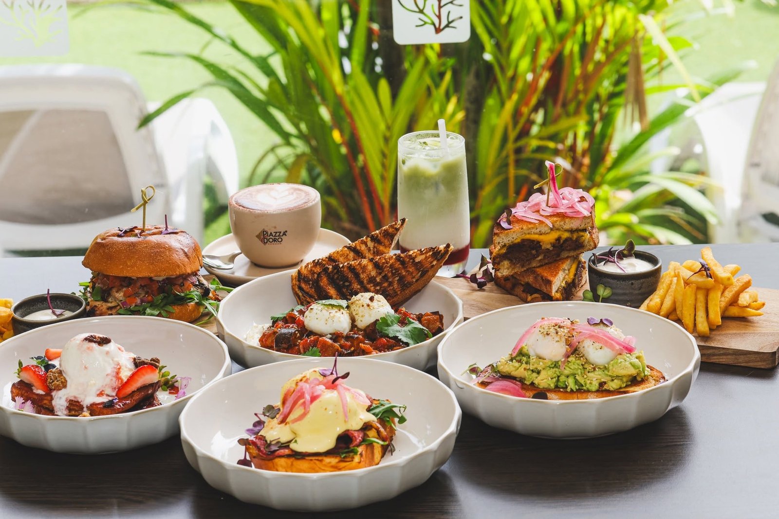 A spread of breakfast dishes on a table surrounded by tropical plants